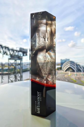 tall thin awards with a black base sitting on a table with Glasgow in the background