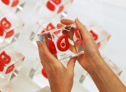 Clear acrylic cube hwith red droplet logo and hurricane text held with 2 hands