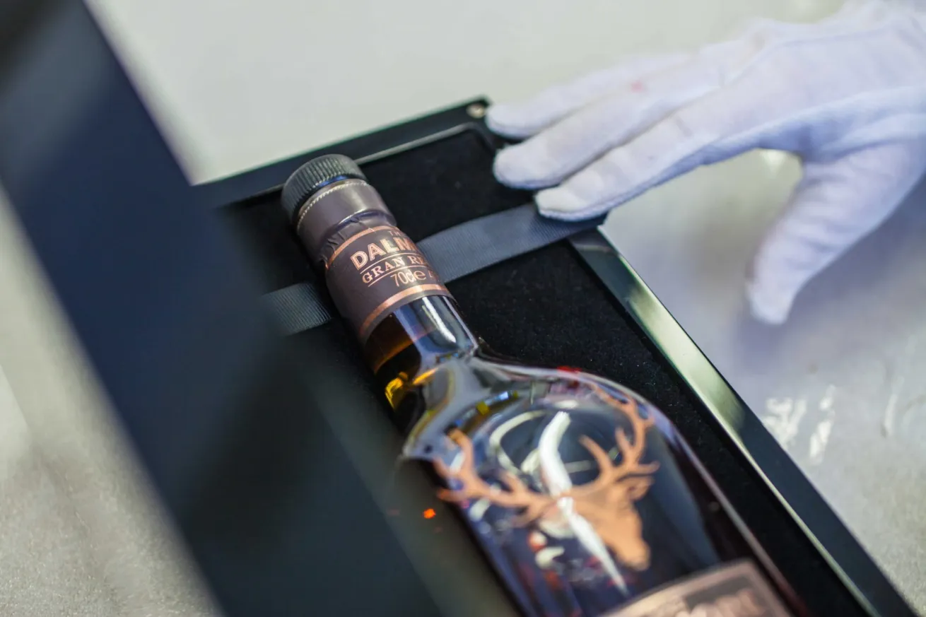 Black Dalmore bottle presentation case open with a black insert, Dalmore whisky bottle and hand in white glove for product displays