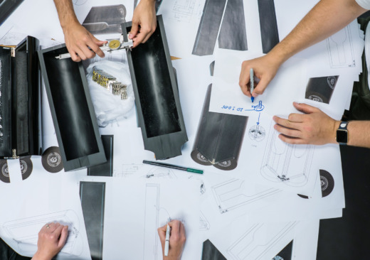 looking down on 3 designers with sketches, CAD concepts and black acrylic prototypes for product displays