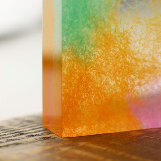 Clear acrylic custom materials samples with green, orange and pink shavings embedded sitting on a wooden base