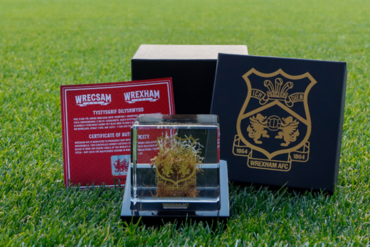 Wrexham AFC limited edition turf cube with certificate of authenticity and black and gold gift box, showcased on the pitch grass.