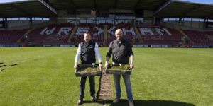Midton directors collecting sections of turf from the Wrexham AFC pitch at the STōK Cae Ras for use in fan merchandise.